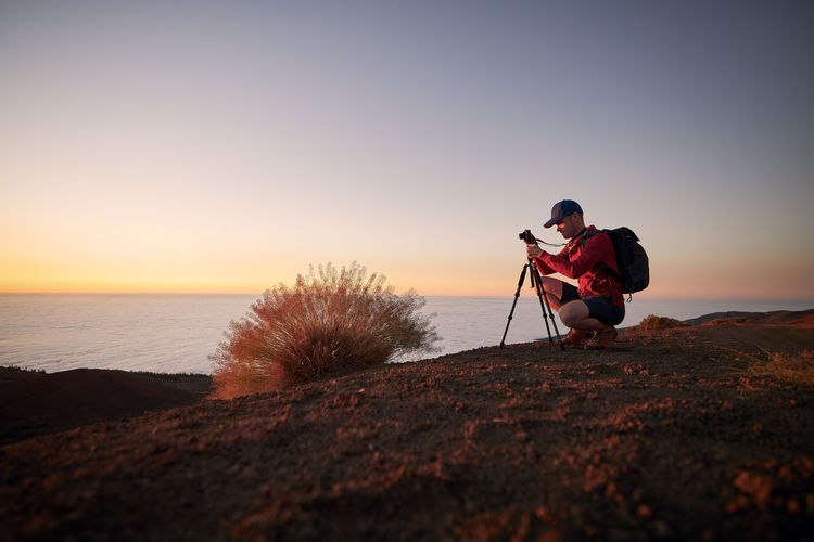 Man during photographing landscape on top of hill above clouds. photographer waiting for sunset.