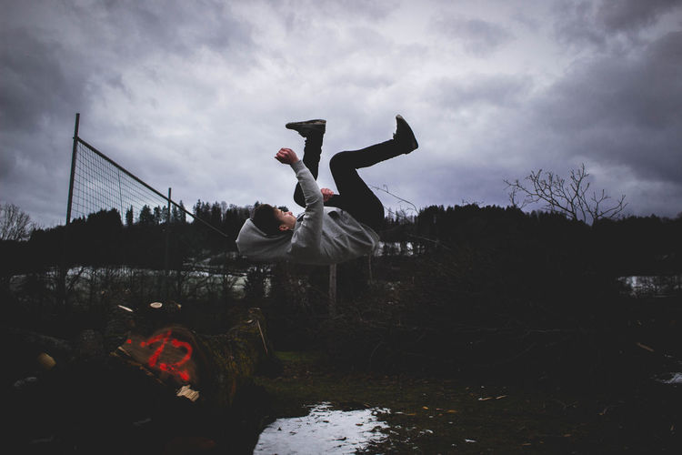 Young man jumping in mid air against cloudy sky