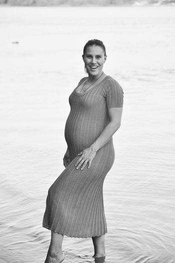 Portrait of smiling pregnant woman standing by sea 