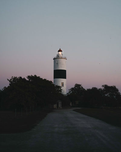 Lighthouse by building against sky during sunset