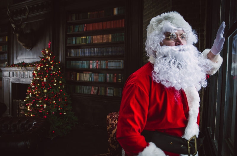 Man wearing santa claus costume standing by window at home