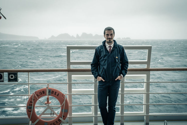 Portrait of man standing on railing against sea