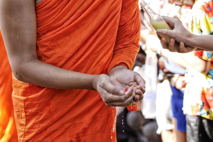 Cropped hand of woman pouring liquid into monk hands outdoors