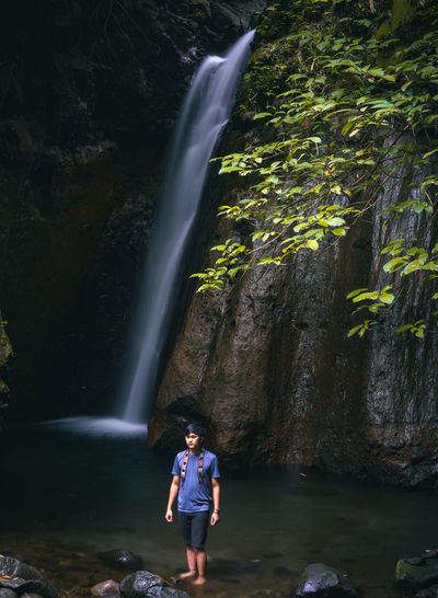 Full length of waterfall standing on rock in forest