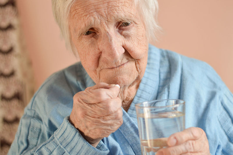  an elderly 90-year-old gray-haired woman who holds a tablet and a glass of water in his hands. 