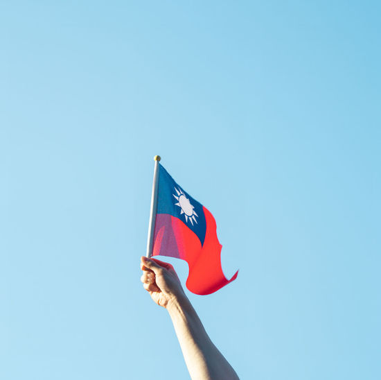 Low angle view of hand holding flag against clear sky