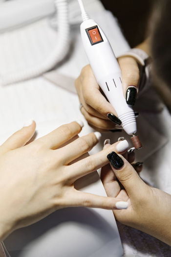 Crop stylist polishing nails of female client over table in salon