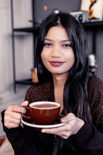 Portrait of woman drinking coffee while sitting in cafe