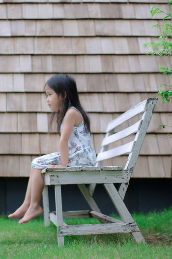 Side view of girl sitting on bench against roof