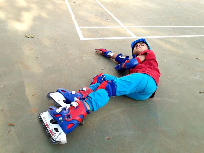 High angle view of fallen boy with inline skates lying on playground