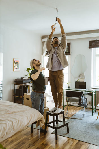 Man installing bulb while standing on stool by boyfriend at home