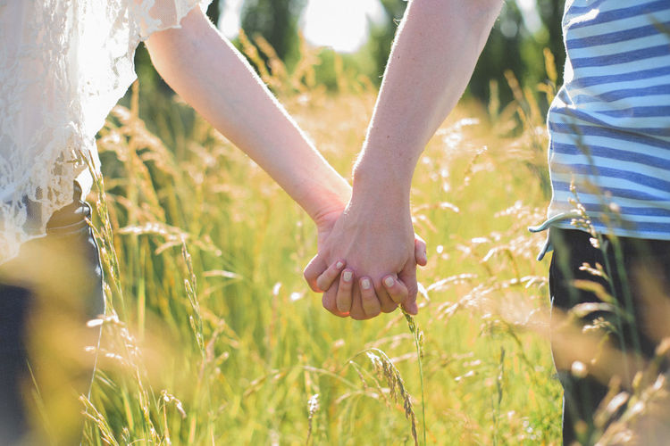 Close-up of couple holding hands on field