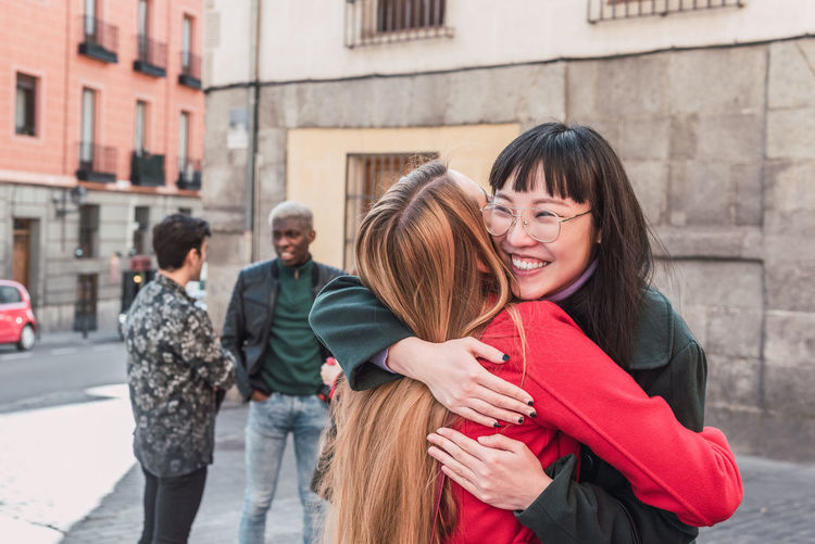 Delighted multiracial female friends hugging while standing on city street and enjoying weekend