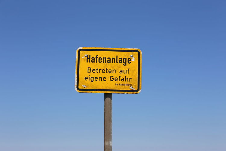 Low angle view of road sign against clear blue sky