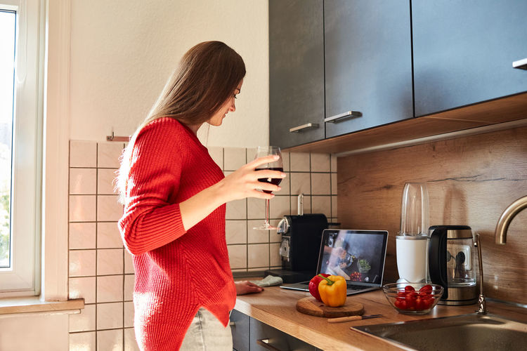 A young woman prepares a salad in the kitchen online and drinks red wine. cooking courses online