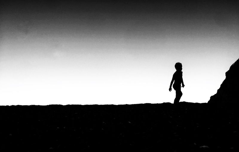 Silhouette boy walking at beach against clear sky