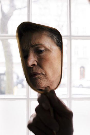 Wrinkled face of senior woman on hand mirror