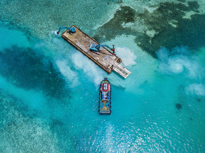 Aerial view of earth movers handling poles on floating platform in male atoll