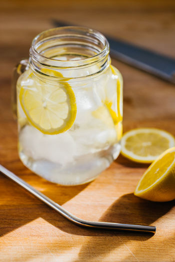 From above metallic reusable straw and glass jug with ice and lemon slices on wooden table in kitchen