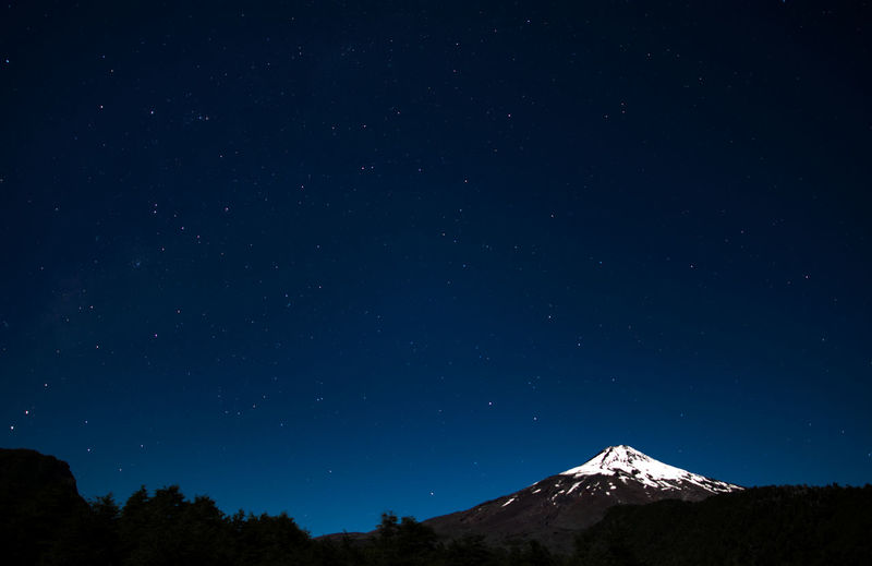 Low angle scenic view of star field over mountain against blue sky during winter