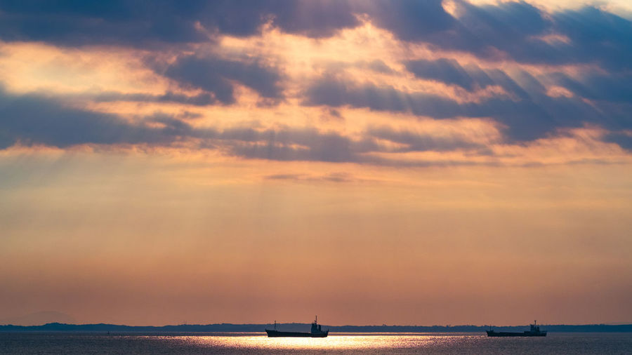 Boat sailing in sea against dramatic sky during sunset