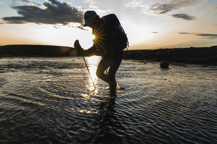 Female backpacker crossing glacial river at sunset in highlands
