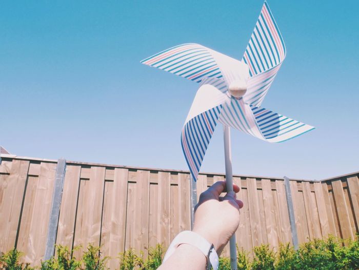 Low angle view of cropped hand holding pinwheel toy against clear sky
