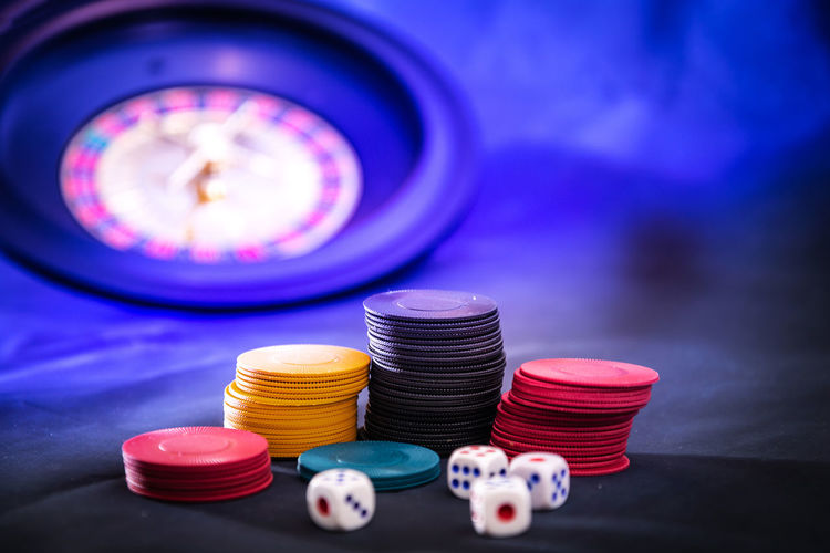 Close-up of colorful gambling chips on table against roulette