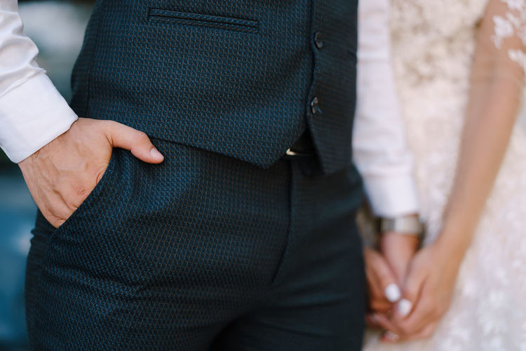 MIDSECTION OF MAN HOLDING WOMAN STANDING BY PEOPLE