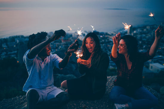 High angle view of happy friends burning sparklers while sitting on mountain at night