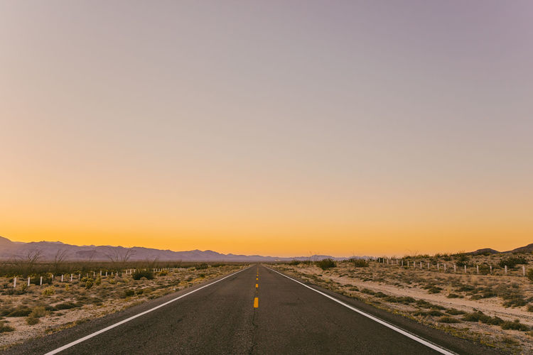 Empty road along landscape at sunset
