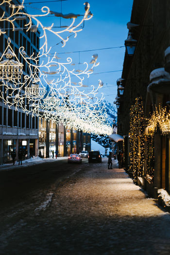 Illuminated street amidst buildings against sky in city during winter