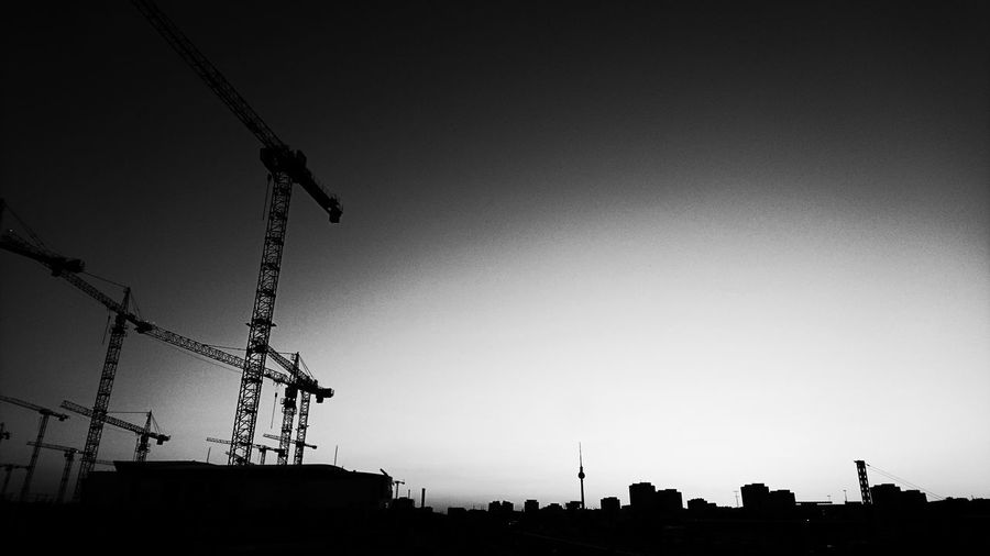 Low angle view of silhouette cranes against clear sky
