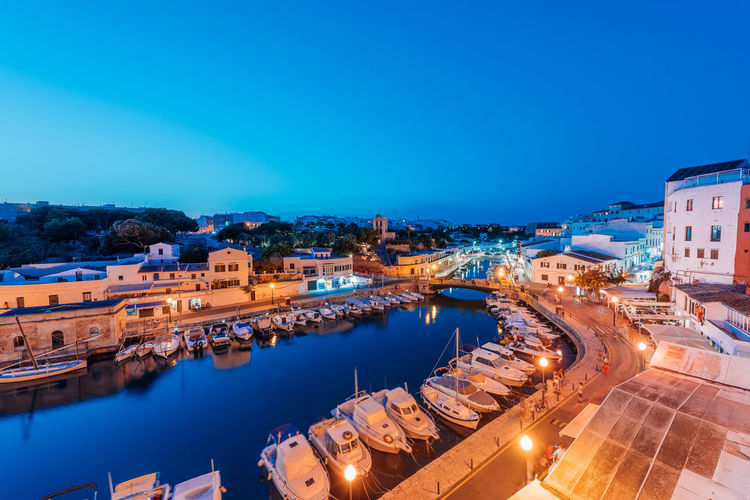 High angle view of illuminated buildings by river against blue sky