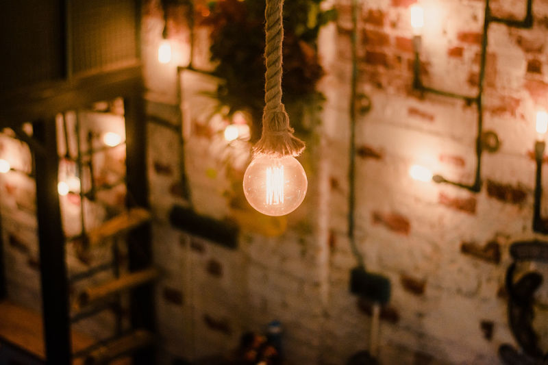 Close-up of illuminated light bulb hanging on rope at night