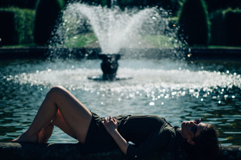 Full length of woman lying against fountain during sunny day