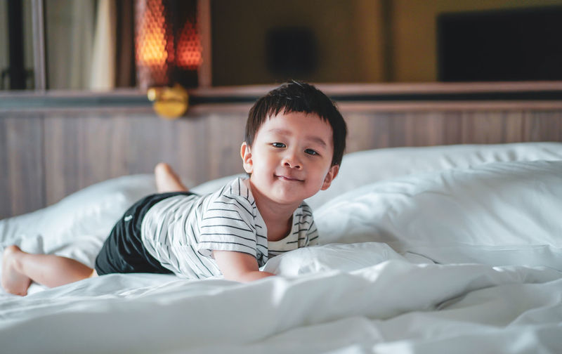 Portrait of little boy wear striped shirt feel relax, laydown on bed, looking at camera. bed vibe.