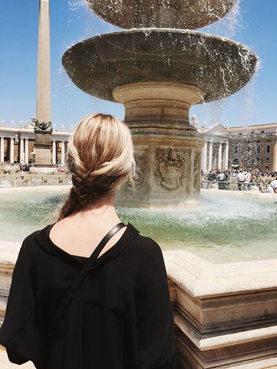 Rear view of woman standing in front of fountain in city