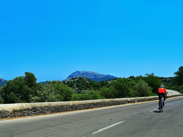 Woman cycling on country road against clear blue sky