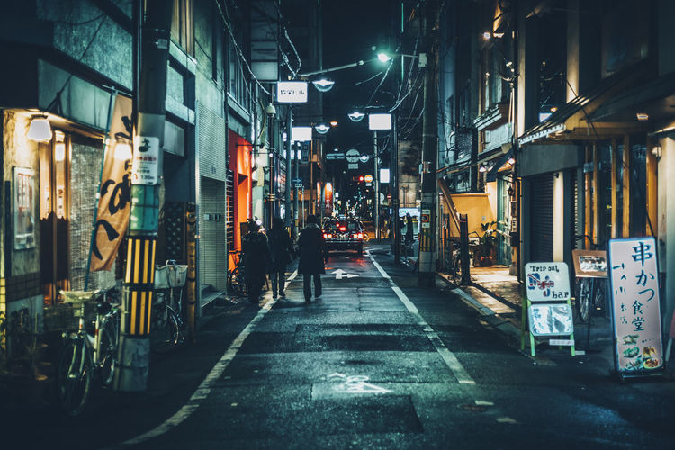 People walking on illuminated city street at night