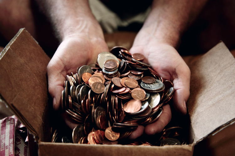 Close-up of man putting us coins in cardboard box
