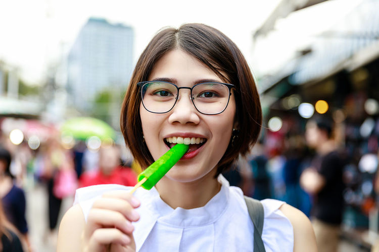 Asian young short hair beautiful woman enjoy eating green popsicle or ice cream at street market
