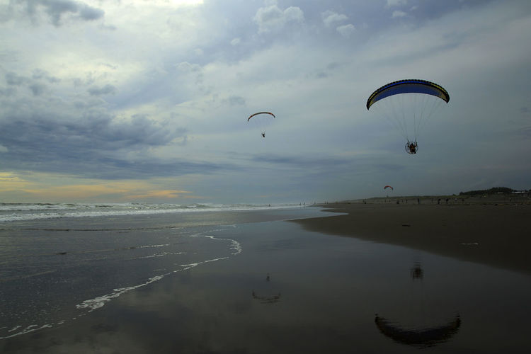 People flying over beach against sky