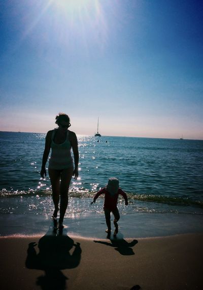 Mother and son wading in sea against sky