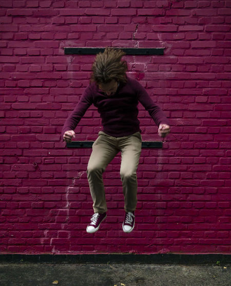 Full length of boy jumping against brick wall