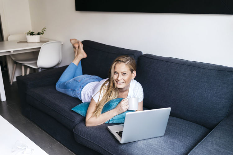 Woman using mobile phone on sofa at home