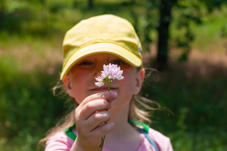 Positive emotional child smiles looks on pink flower in hand. cheerful pretty girl in yellow cap.
