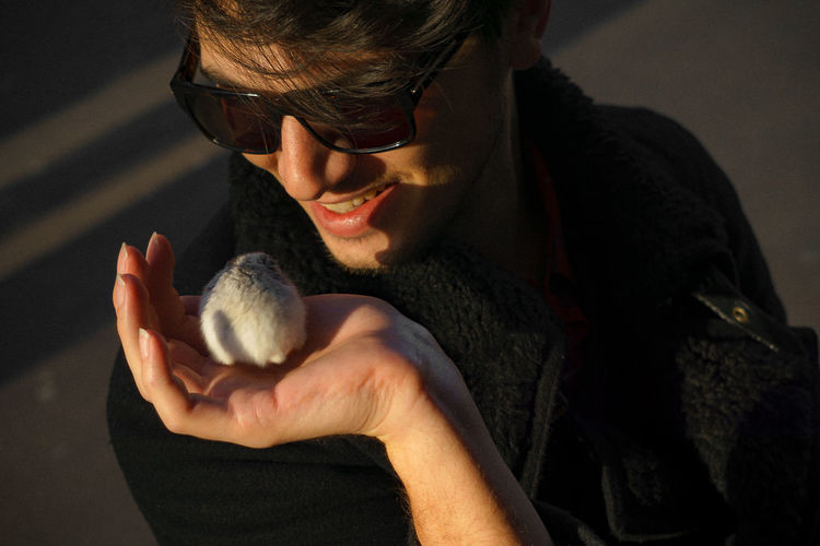 Smiling young man wearing sunglasses while holding hamster
