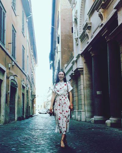 Portrait of young woman on alley amidst buildings
