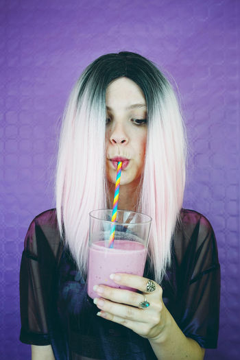 Young woman drinking smoothie while standing against wall